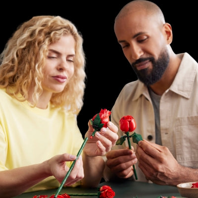 Two people holding red LEGO roses against a black background