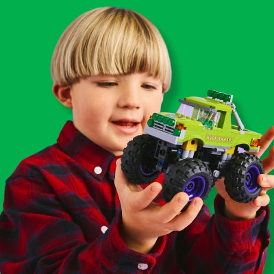 Child holding a toy monster truck against a green background