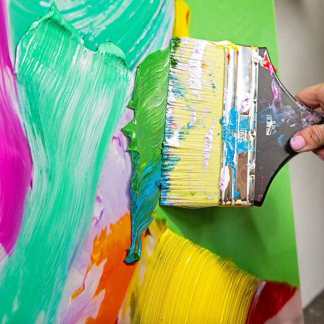 Green Liquitex Heavy Body Acrylic Paint being painted on a canvas covered in other colours with a paint brush