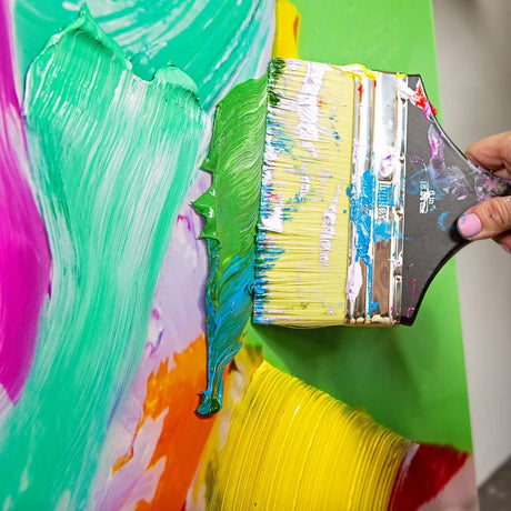 Green Liquitex Heavy Body Acrylic Paint being painted on a canvas covered in other colours with a paint brush