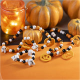 Halloween-themed beaded bracelets with ghost and pumpkin charms on an orange surface with pumpkins and a candle in the background.