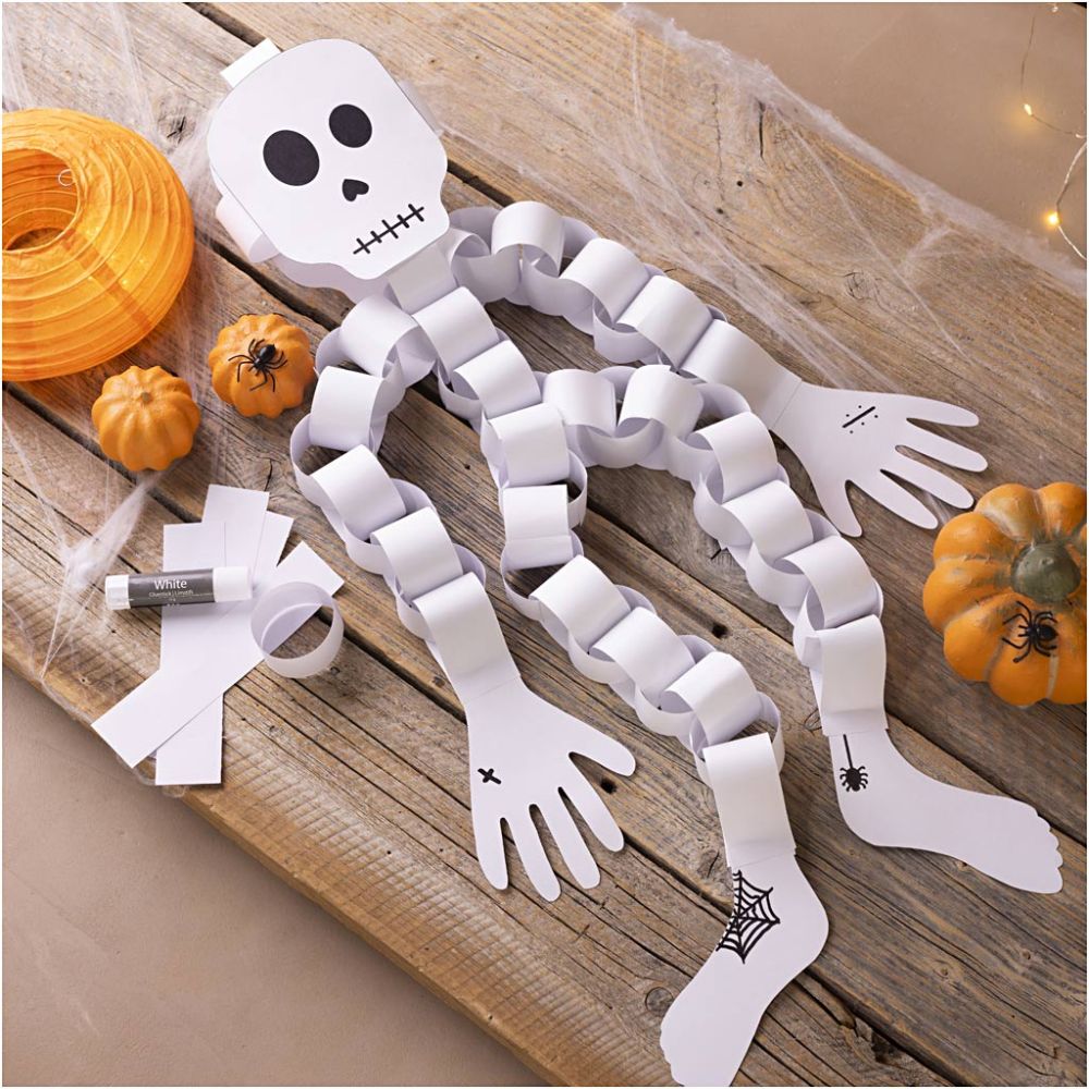 Paper skeleton craft on a wooden surface with pumpkins and string lights.