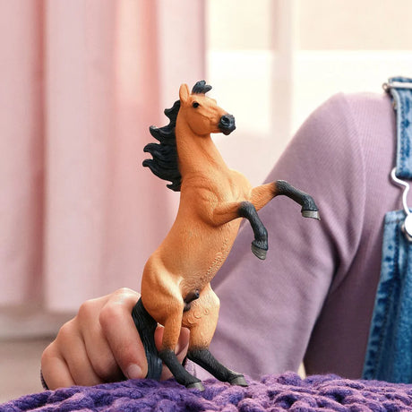Hand holding a toy horse on a purple surface with a blurred background
