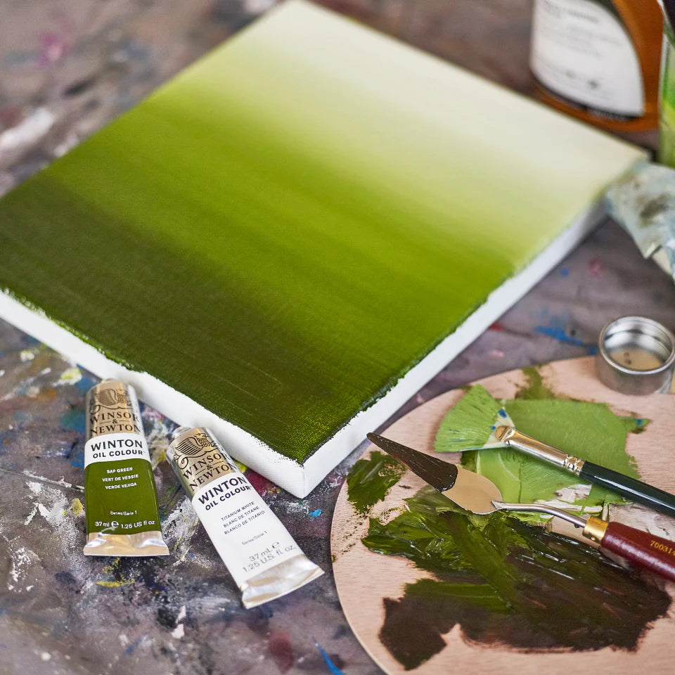 Artistic setup with green painting on canvas, Winton oil color tubes, and painting tools on a table.