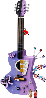 A purple and lavender toy guitar with various colorful accessories and small character figures, shown against a solid green background.