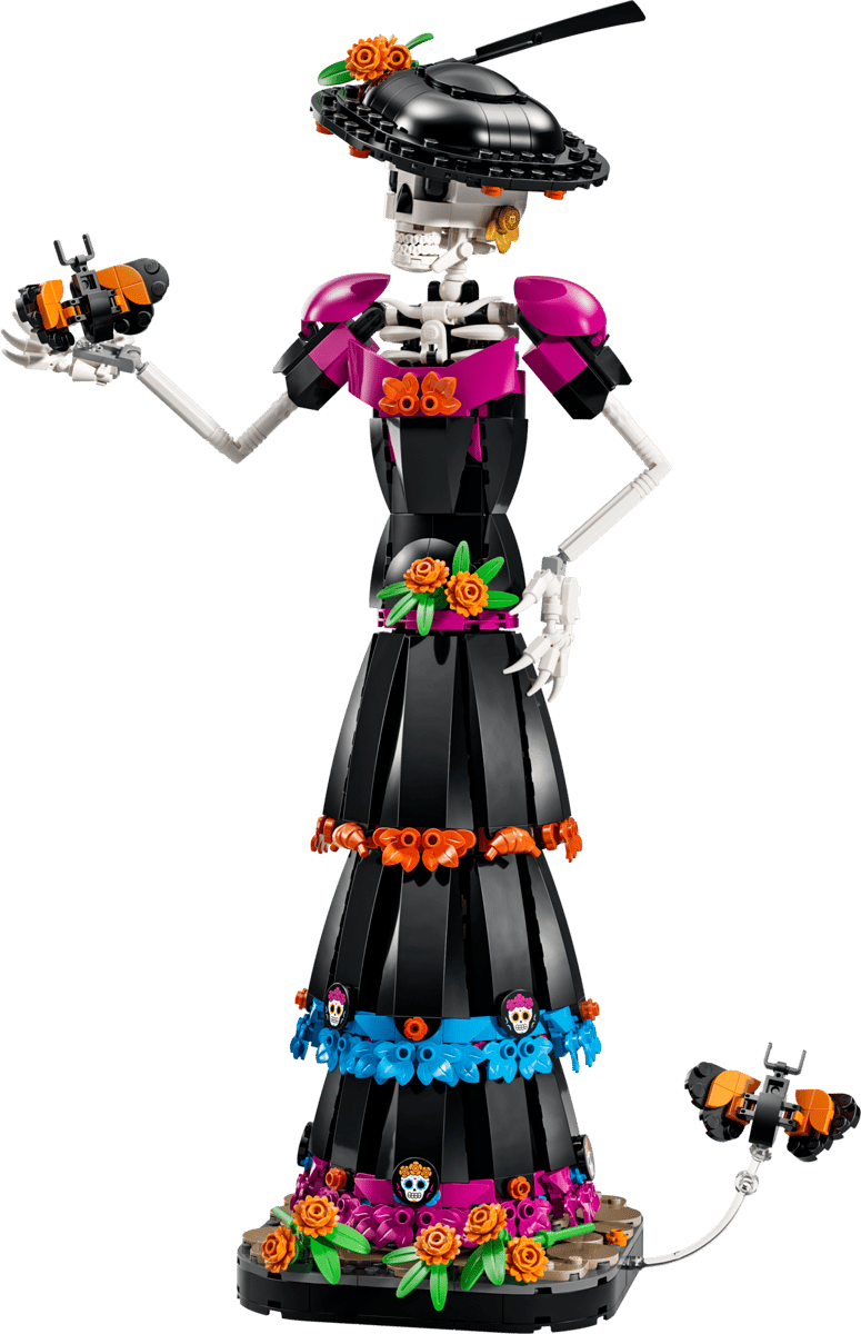 A Day of the Dead skeleton figurine built from LEGO, featuring a black dress with pink, orange, and blue floral accents, a black hat with flowers, and skull details, shown against a solid green background.