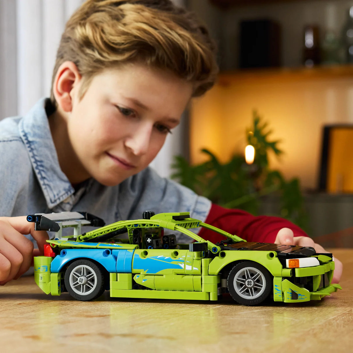 Child playing with a green toy car made of interlocking bricks on a wooden table.