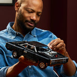Man holding a detailed model of a car, possibly a toy or model vehicle, against a dark background.