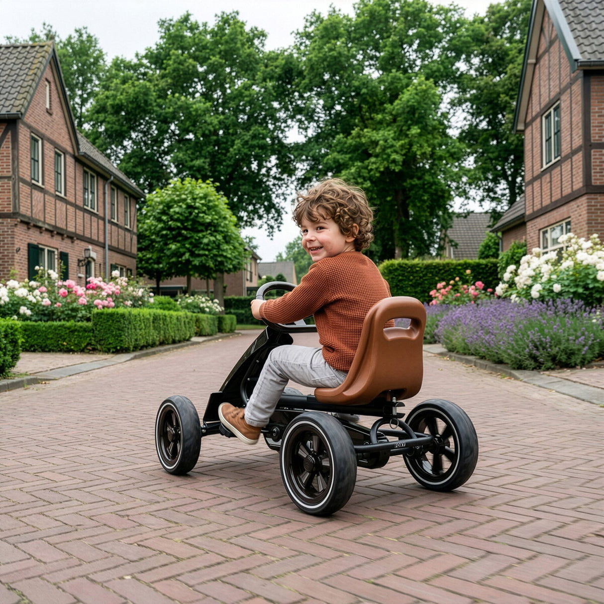 Child riding a pedal car on a brick driveway with houses and greenery in the background
