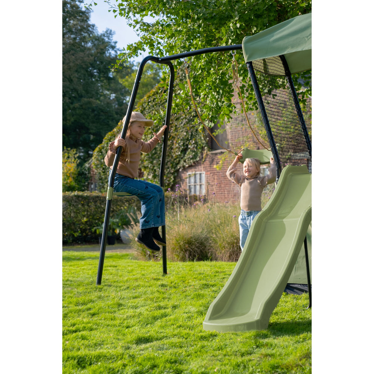 Children playing on a swing set with a slide in a garden.