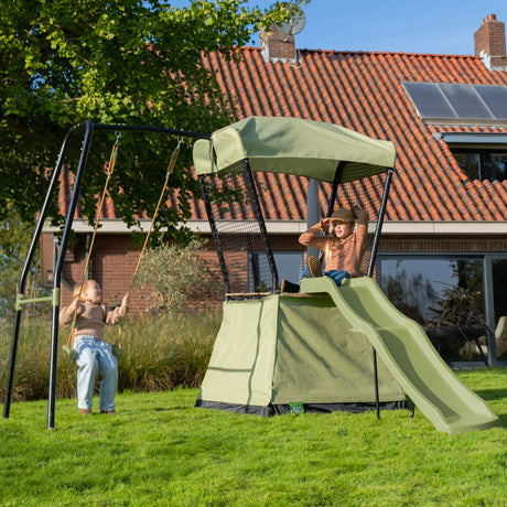 Children playing on a swing set with slide and canopy in a backyard.