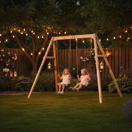 Two children on a swing set in a backyard with string lights and flowers.