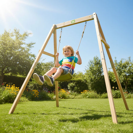 Child swinging on a wooden swing set in a garden with trees and flowers in the background.
