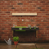 Play kitchen set against a brick wall with a small plant and watering can on the ground.