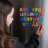 Person interacting with colorful magnetic letters on a refrigerator door.