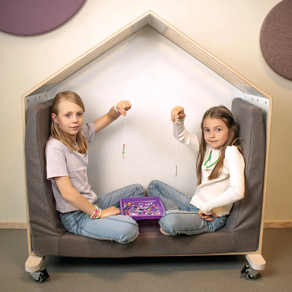 Two children playing inside a house-shaped playhouse with a purple box on a gray floor.