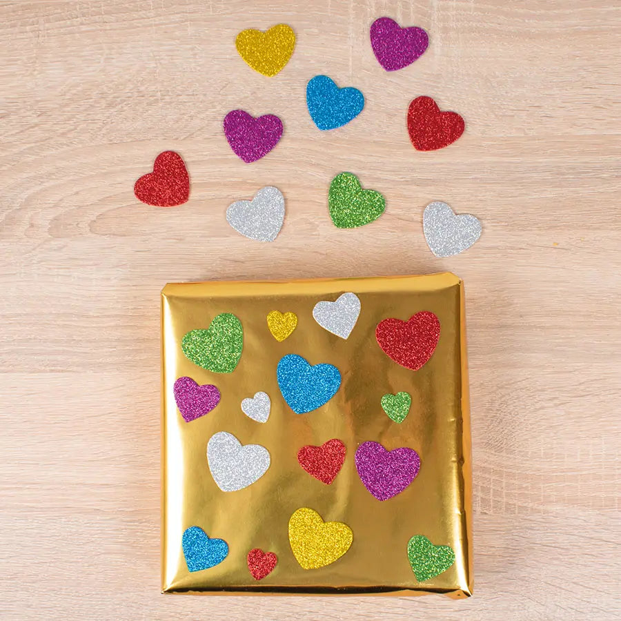 Gold gift wrap with colorful heart stickers on a wooden surface