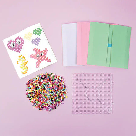 Crafting materials including beads, paper templates, and a pegboard on a pink background