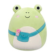 A plush frog toy with a light green body, cream-colored belly, black embroidered eyes and smile, pink cheeks, and a teal pouch belt with a small pink flower accent, shown on a plain white background.