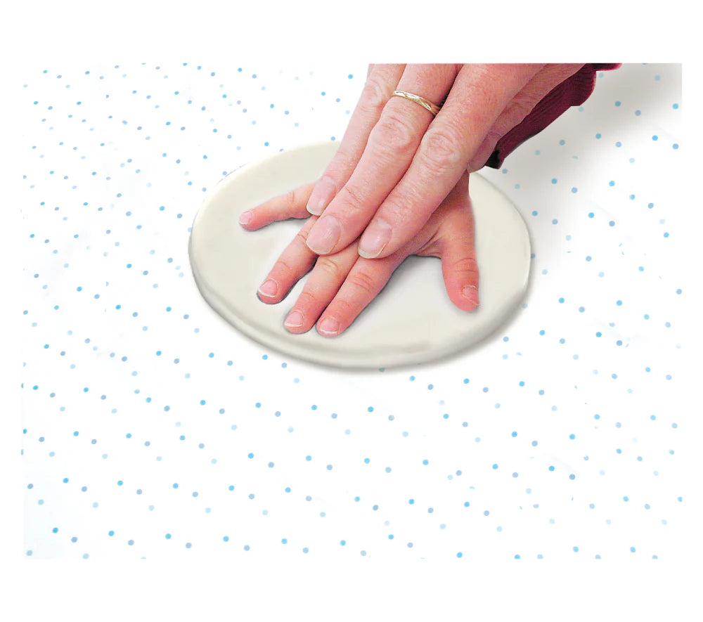 Hand pressing a round piece of clay on a white surface with blue dots